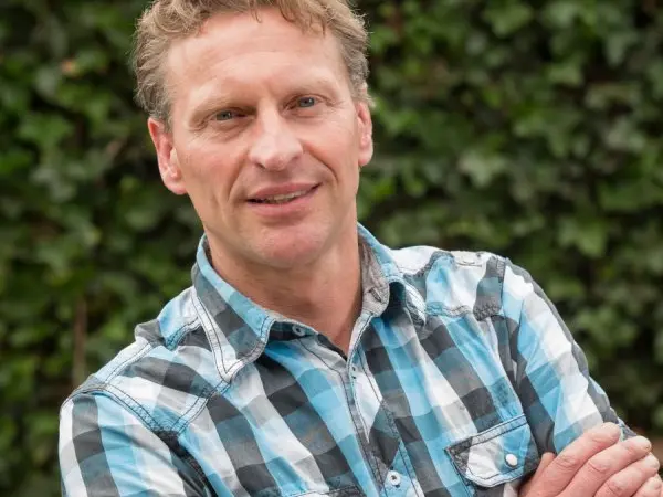 Portret van een lachende man met geruit overhemd voor een klimopwand