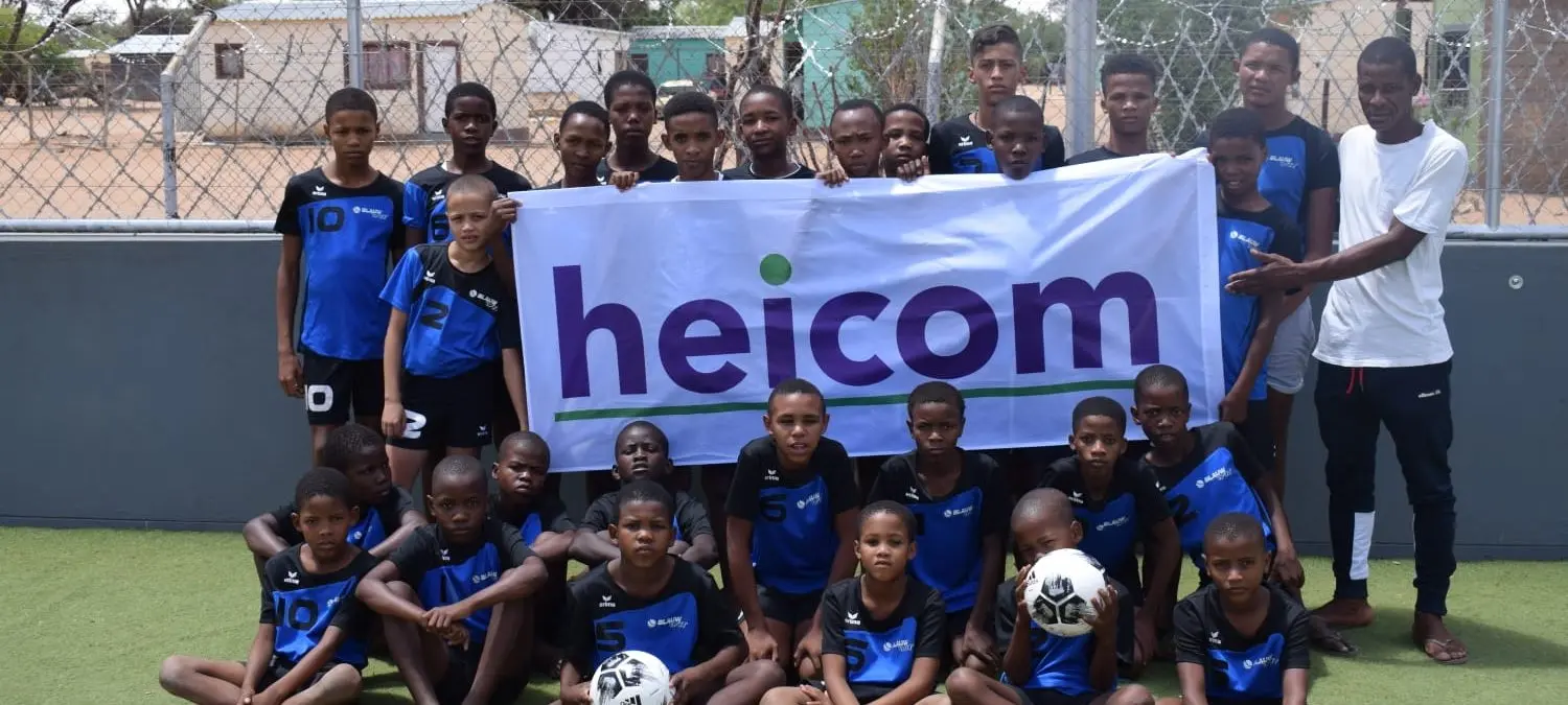 Groep kinderen in voetbaltenue houdt een Heicom-spandoek vast