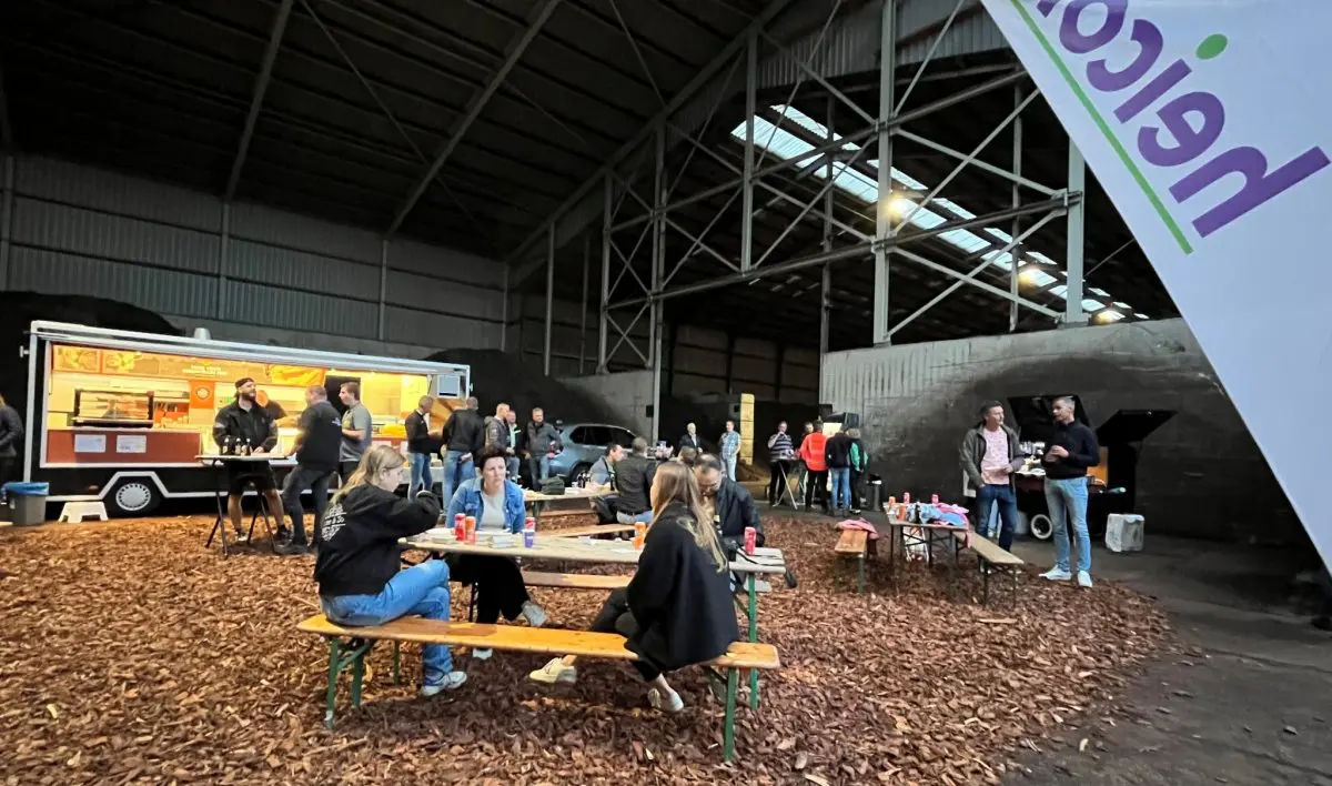 Bezoekers aan picknicktafels op houtsnippers in een loods met foodtruck