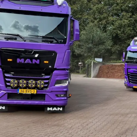 Twee paarse Heicom-vrachtwagens op een erf, vooraan een nieuwe MAN-trekker