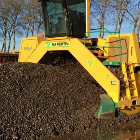 Gele compostkeerder keert een lange donkere composthoop om