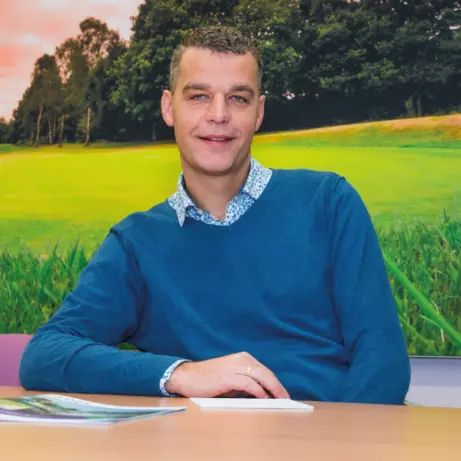 Man in blauwe trui aan tafel voor een wandfoto van een golfbaan