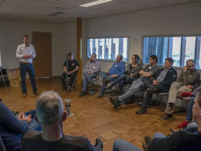 Man staat te praten voor een kring zittende deelnemers in een zaaltje