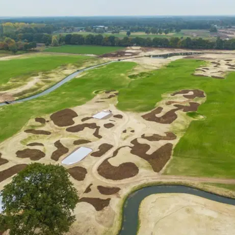 Luchtfoto van een golfbaan in aanleg met zandbunkers en een sloot