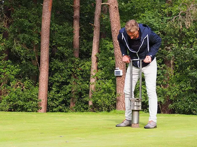 Man boort met een steekboor een grondmonster uit een golfgreen