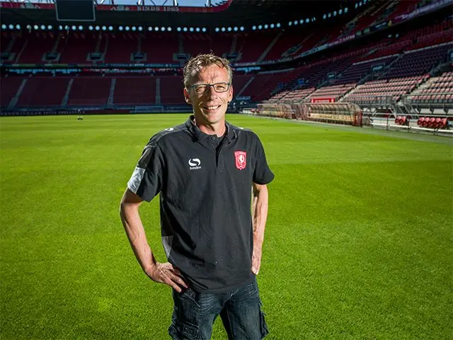 Man in clubpolo poseert op het veld van een leeg voetbalstadion
