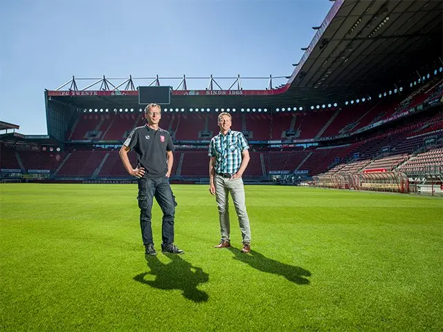 Twee mannen staan op het grasveld van een leeg voetbalstadion