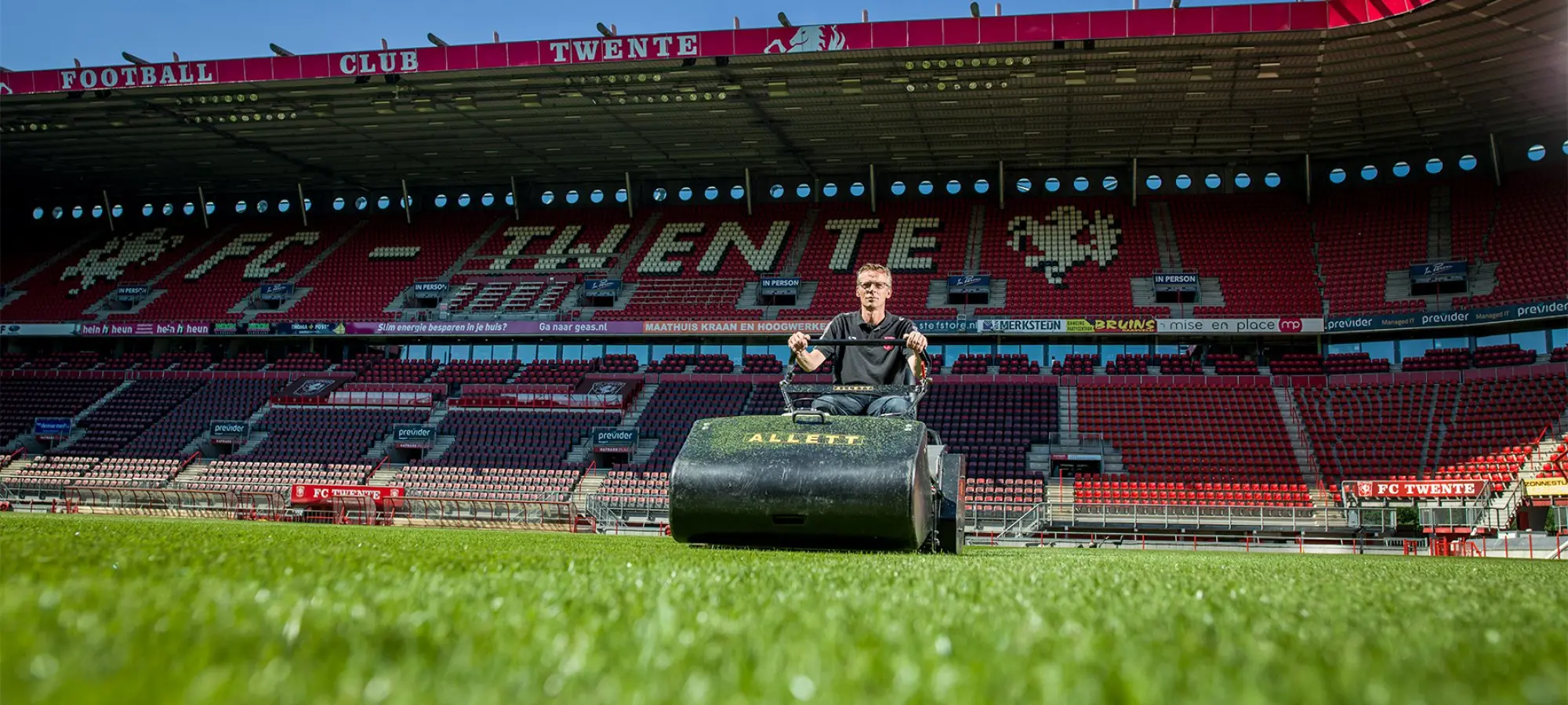 Terreinknecht op een maaimachine op het gras van een leeg voetbalstadion