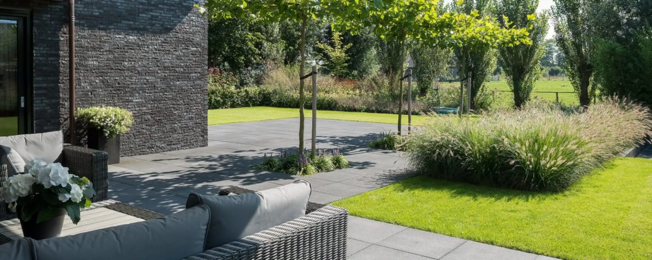 Loungebank op een terras met gazon en siergrassen in een tuin