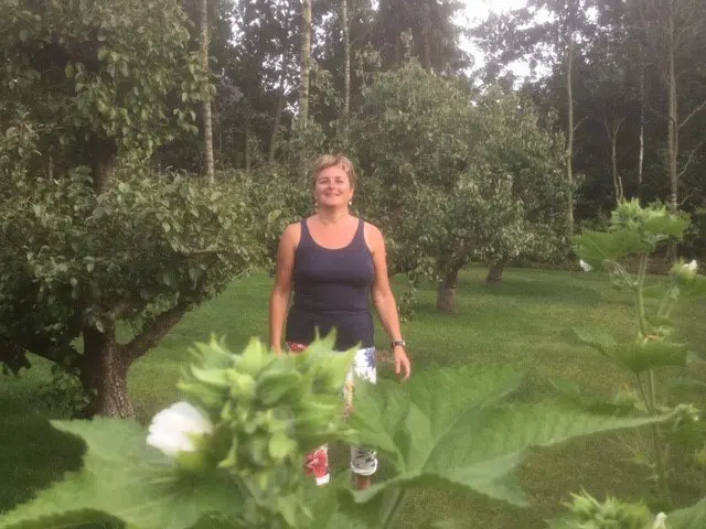 Vrouw staat glimlachend in een boomgaard tussen fruitbomen en groen