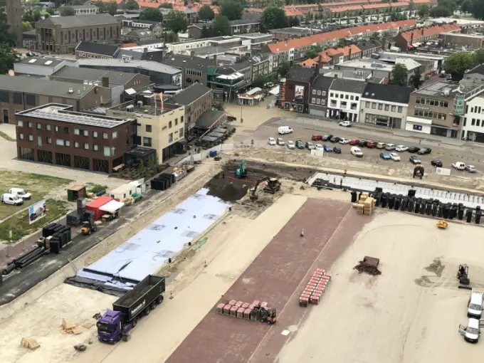 Bouwterrein in een dorpscentrum van bovenaf, met kratten en vrachtwagen